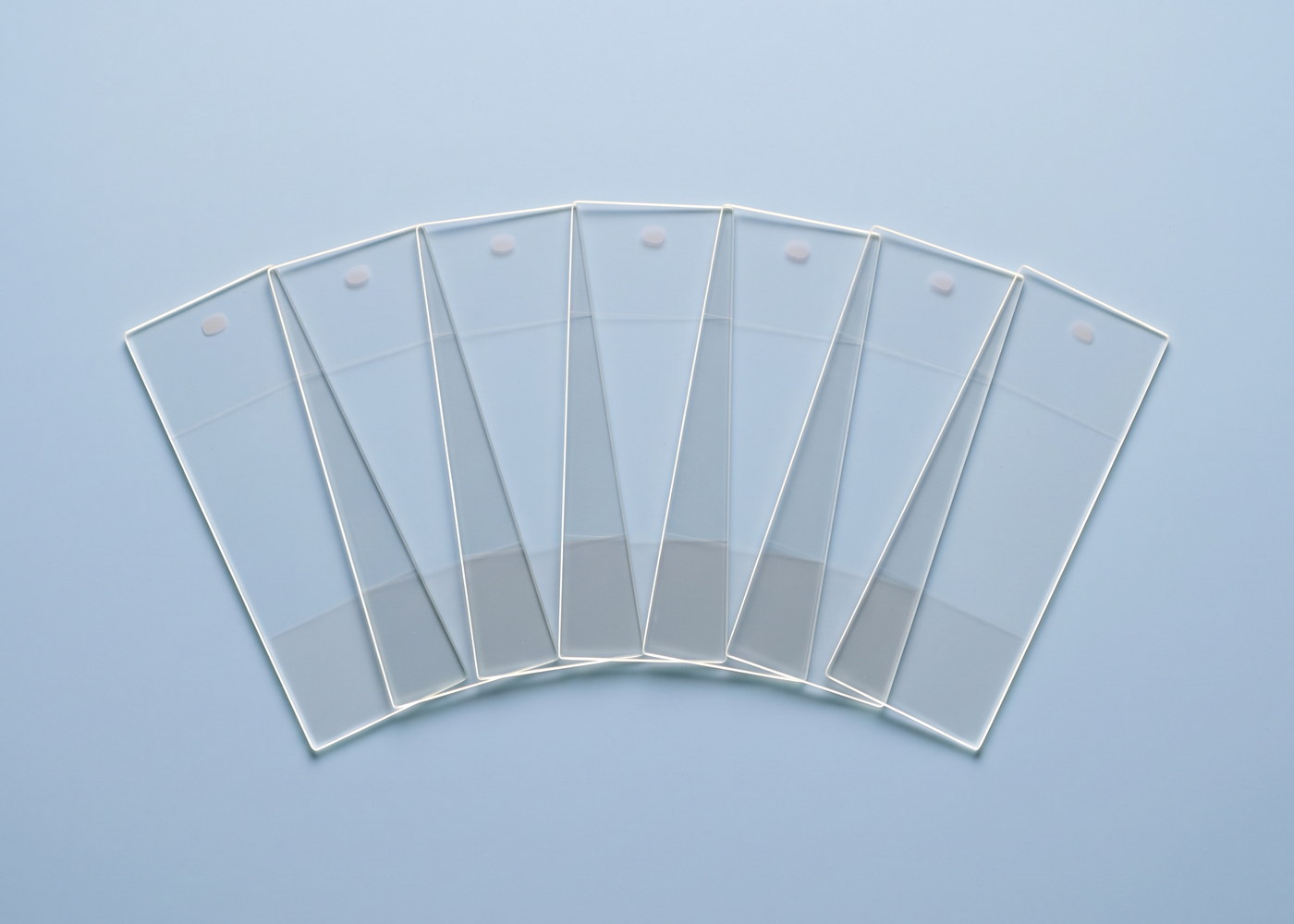 Sieben Objektträger aus Glas, aufgefächert und von hinten beleuchtet, die Glaskanten leuchten auf