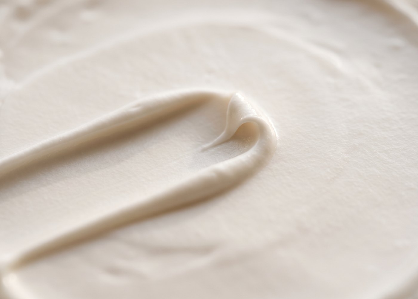 Makroaufnahme einer weißen Creme, ein Spatelzug hat eine weiche Spur in die glatte Oberfläche gezogen