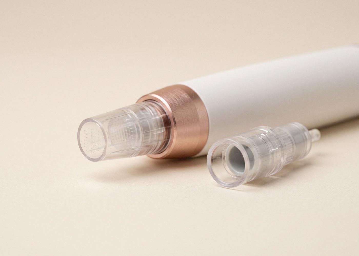 Vorderes Ende eines Microneedling-Pens mit aufgesetztem klarem Aufsatz, daneben ein zweiter unbenutzter Aufsatz