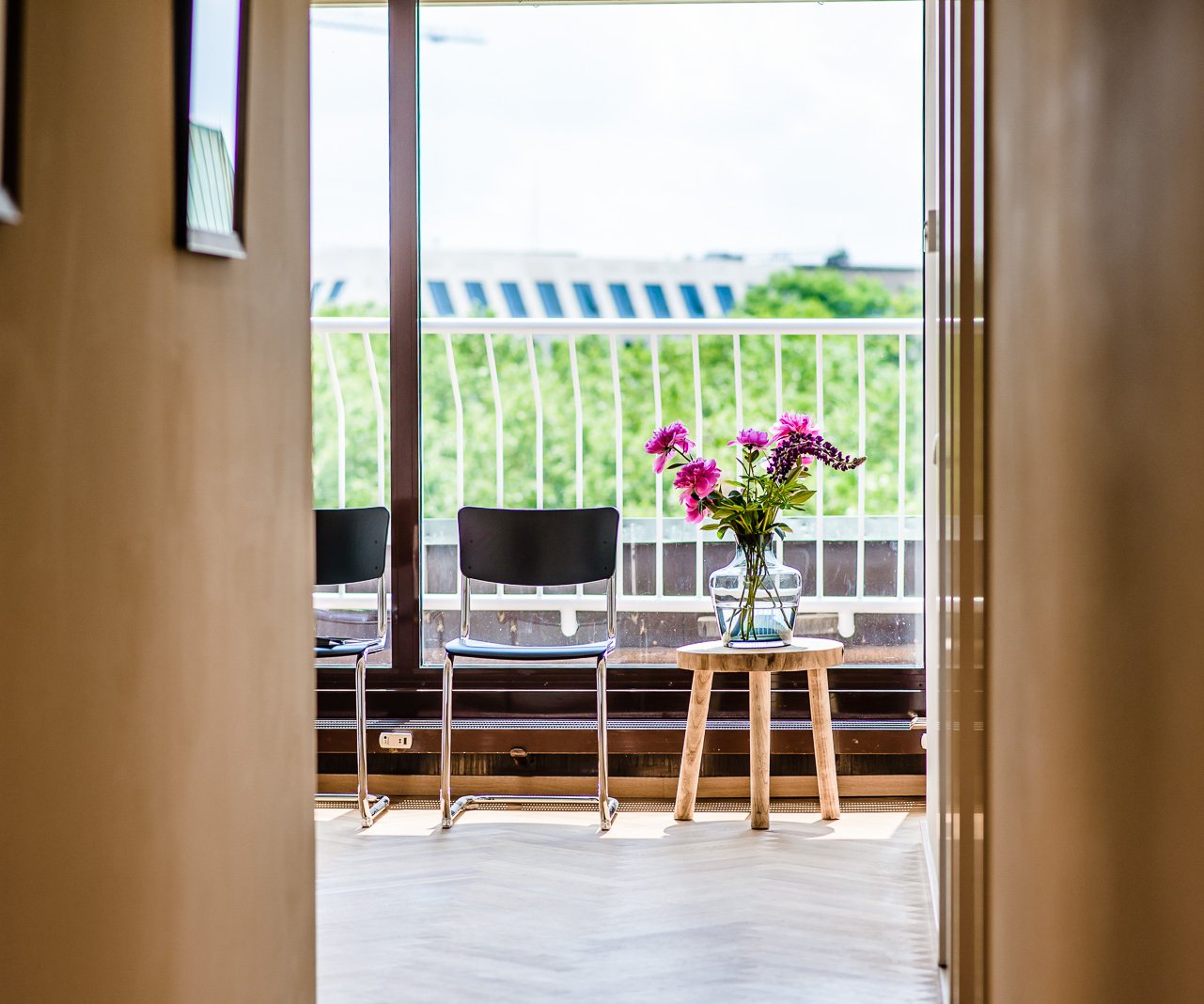 Blick durch die offene Tür auf die Dachterrasse, zwei Stühle und Blumen auf einem Hocker