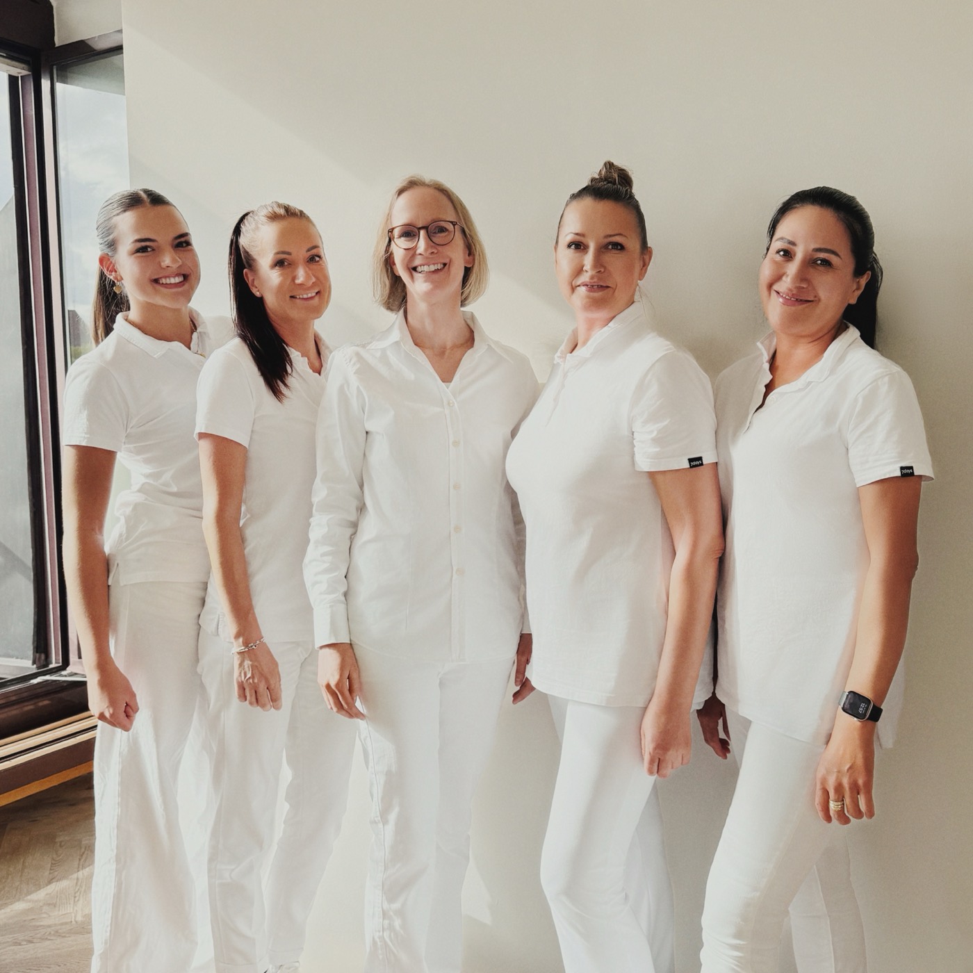 Das Praxisteam mit Dr. med. Regina Ramesohl in der Mitte, fünf Frauen in weißer Kleidung vor heller Wand