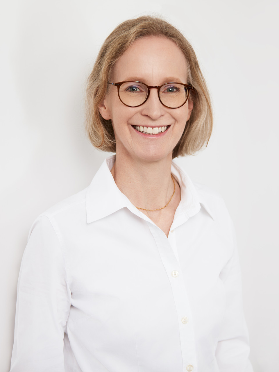 Porträt von Dr. med. Regina Ramesohl in weißer Bluse, lächelnd vor heller Wand